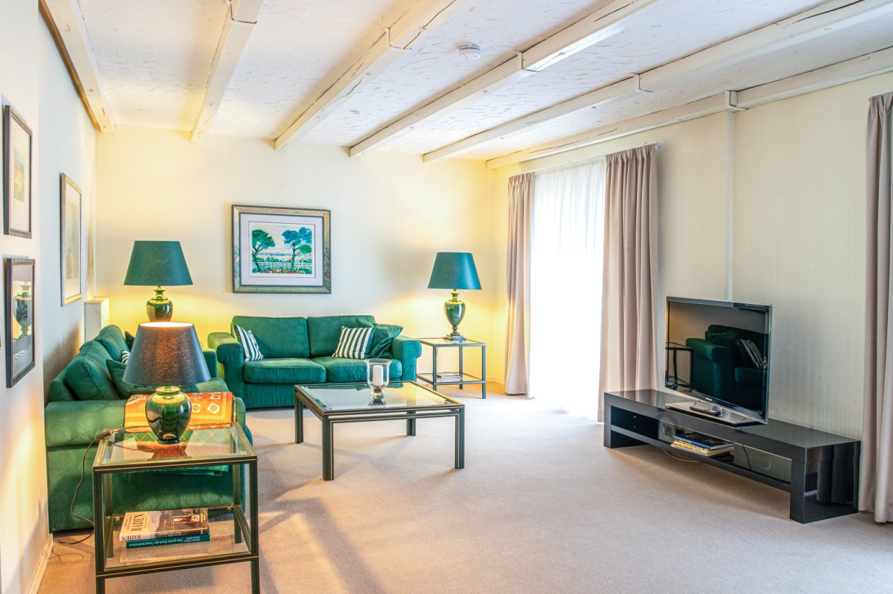 Lichtdurchflutetes Wohnzimmer mit eleganten Deckenbalken und harmonischer Grünakzentuierung Lichtdurchflutetes Wohnzimmer mit eleganten Deckenbalken und harmonischer Grünakzentuierung