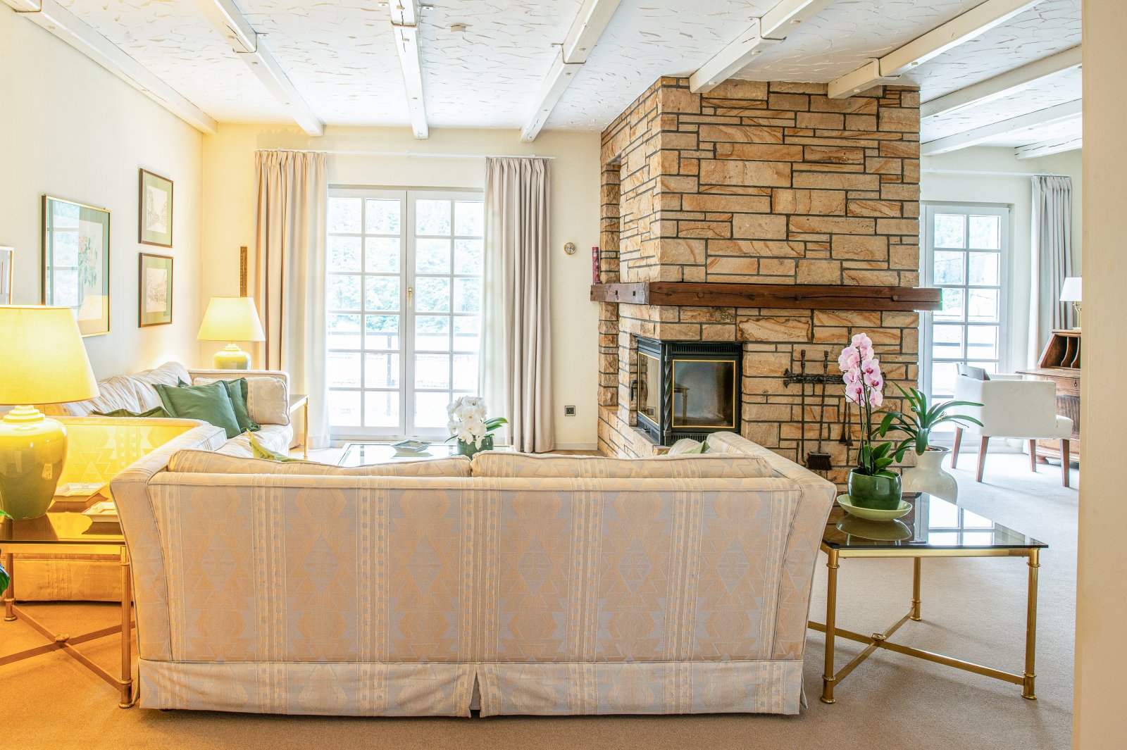 Gemütlicher Wohnbereich mit rustikaler Naturstein-Kaminwand und lichtdurchfluteten Panoramafenstern Gemütlicher Wohnbereich mit rustikaler Naturstein-Kaminwand und lichtdurchfluteten Panoramafenstern